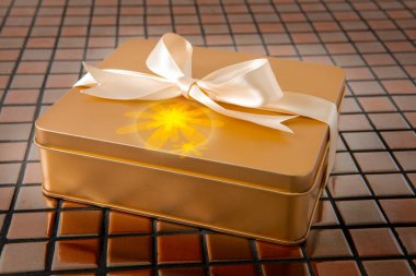 Altın hediye kutusu arkaplanda saten kurdeleyle bağlanmış.