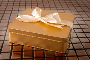 Altın hediye kutusu arkaplanda saten kurdeleyle bağlanmış.