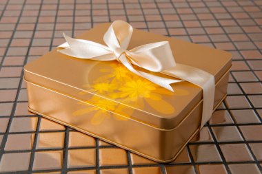 Altın hediye kutusu arkaplanda saten kurdeleyle bağlanmış.