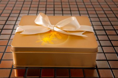 Altın hediye kutusu arkaplanda saten kurdeleyle bağlanmış.