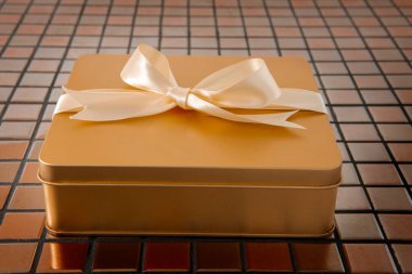 Altın hediye kutusu arkaplanda saten kurdeleyle bağlanmış.