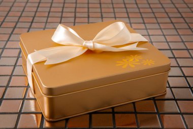 Altın hediye kutusu arkaplanda saten kurdeleyle bağlanmış.