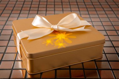 Altın hediye kutusu arkaplanda saten kurdeleyle bağlanmış.