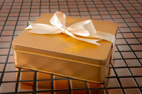 Altın hediye kutusu arkaplanda saten kurdeleyle bağlanmış.