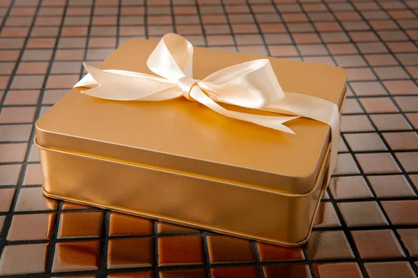 Altın hediye kutusu arkaplanda saten kurdeleyle bağlanmış.