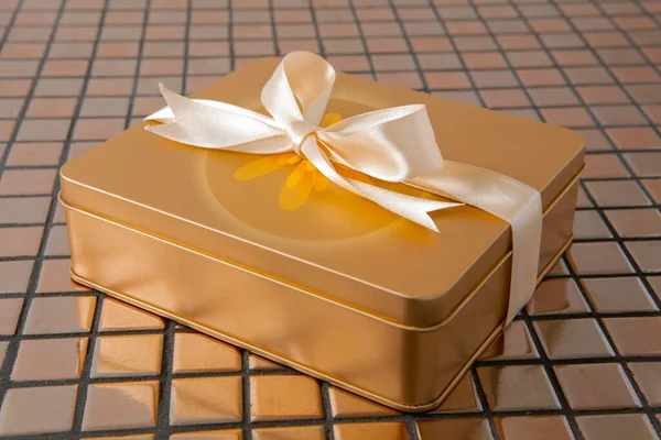 Altın hediye kutusu arkaplanda saten kurdeleyle bağlanmış.