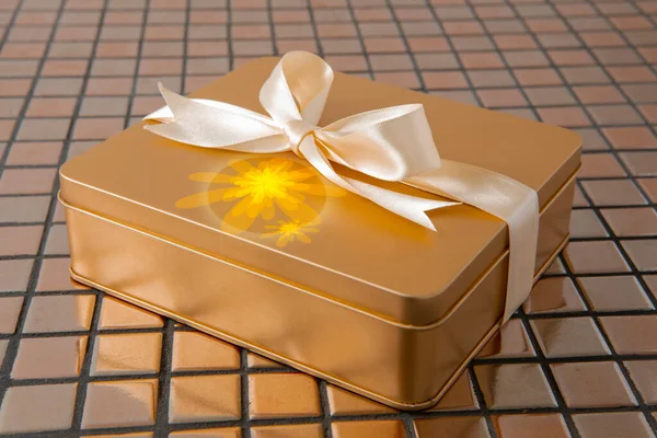 Altın hediye kutusu arkaplanda saten kurdeleyle bağlanmış.
