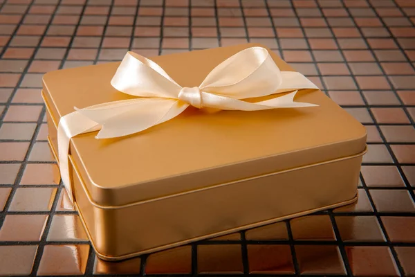 Altın hediye kutusu arkaplanda saten kurdeleyle bağlanmış.