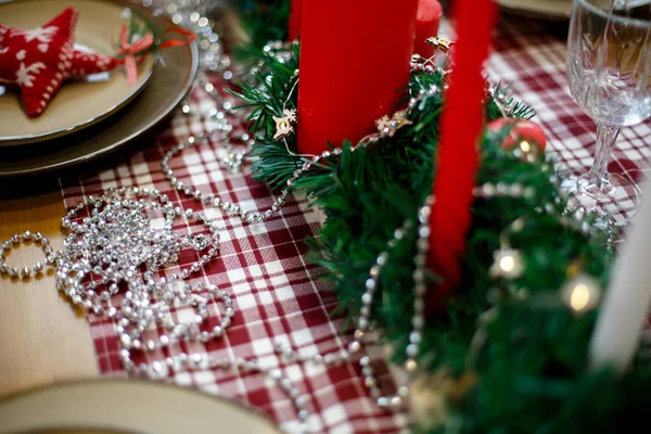 Red candles in green tinsel on a red checkered tablecloth — Stock Photo, Image