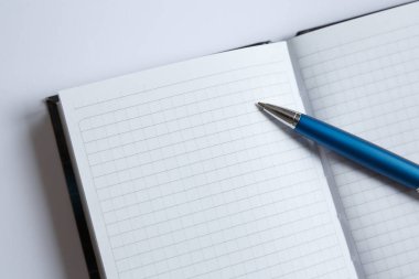 Mavi bir kalem siyah bir defterin beyaz bir sayfasında yatıyor. Açık kare okul not defteri düz yatıyordu