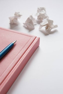 Pembe günlük ve beyaz arka planda mavi metal kalem, buruşmuş kağıt parçaları. Mektuptaki hatalar