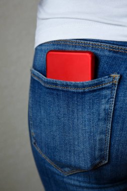 Mavi kotun arka cebindeki kırmızı akıllı telefon. Yaklaş.