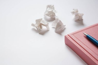 Pembe günlük ve beyaz arka planda mavi metal kalem, buruşmuş kağıt parçaları. Mektuptaki hatalar