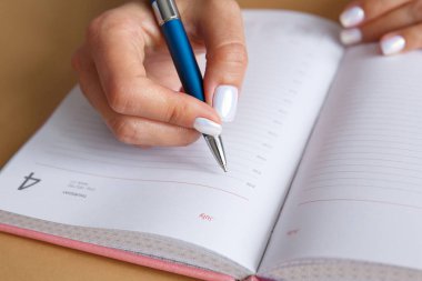 Pembe bir günlükte mavi gümüş kalemle yazan bir kadın. Günlük planlama. İş kadını iş günü planı yapar..