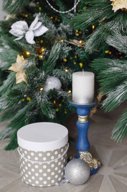 Noel kartı. Beyaz mumlu mavi şamdan. Noel ağacının altında bir hediye kutusu. Karda ladin dalları. Noel süslemeleri.