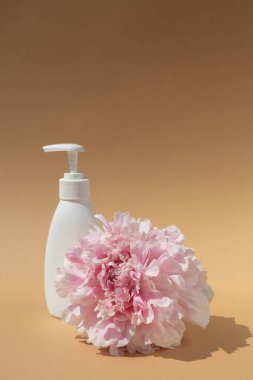 Kahverengi arka planda beyaz kozmetik şişesi ve pembe şakayık tomurcuğu. Deri hidrasyonu ve sağlık.