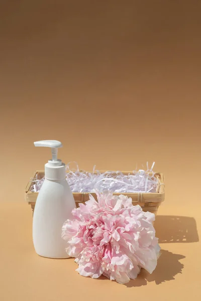 White bottle and wicker basket. Large bud of pink peony. Cosmetics and perfumery. Body and skin care. Spa concept, massage. Place for your text.