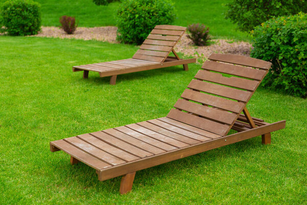 Реклама отдыха и туризма. Два пустого коричневого деревянного шезлонга или шезлонга, на зеленой траве свежего газона