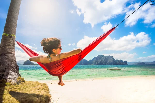 Młoda kaukaska kobieta relaksująca się w czerwonym hamaku na tropikalnej plaży — Zdjęcie stockowe