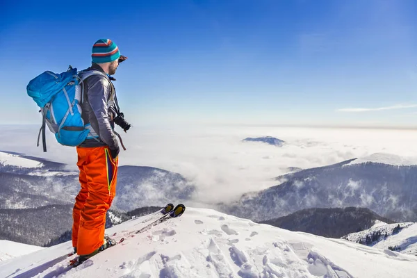 Jovem homem ativo admirando a vista do vale de um cume enquanto esquia — Fotografia de Stock