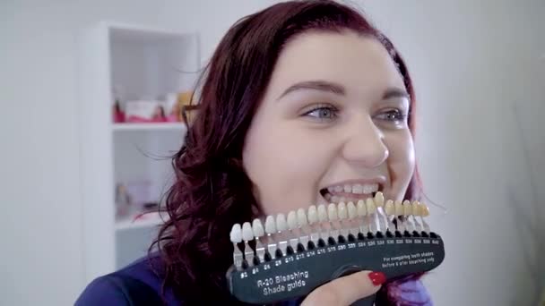 Menina bonita com amostras de cor de dente escolhendo a cor dos dentes — Vídeo de Stock
