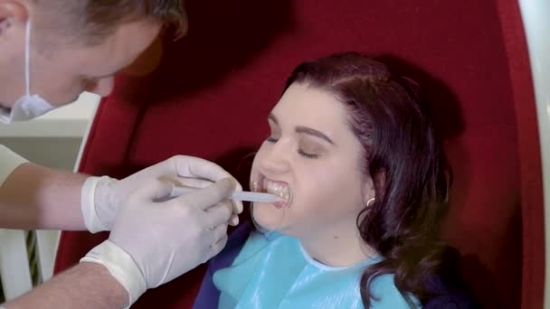Стоматолог наносит на пациента гель для отбеливания зубов — стоковое видео