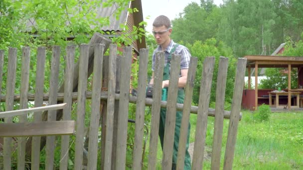 Man Green Jumpsuit Goggles Sawing Electric Saw Chainsaw Old Fence — Stock Video