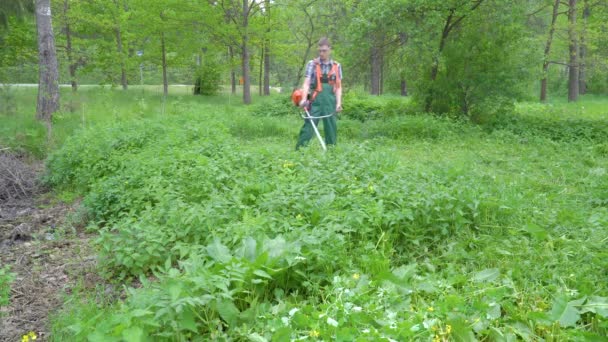 緑のジャンプスーツとゴーグルの労働者は ガソリンポンプで草を刈ります — ストック動画