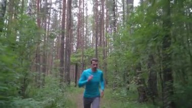 Yavaş çekim gri şortlu beyaz atlet ve ormanda koşan mavi uzun kollu sağlıklı yaşam tarzı kavramı.