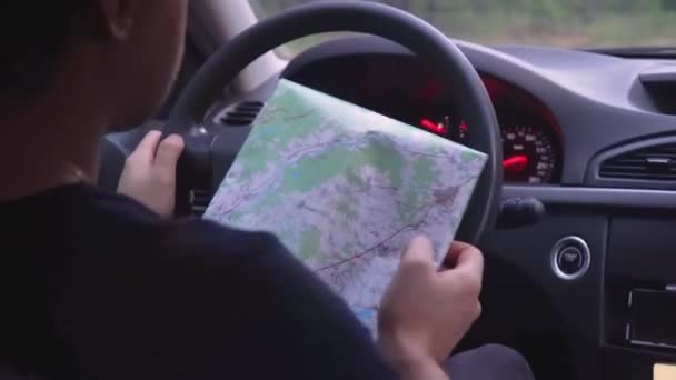 Мужчина управляет машиной, глядя на бумажную карту — стоковое видео