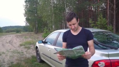 Haritalı beyaz adam ormanda arabanın yanında duruyor.