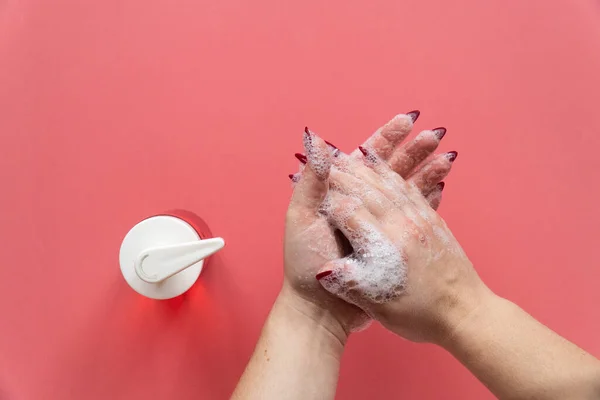 Woman soaps hands with liquid soap on pink background. Personal care concept before meals