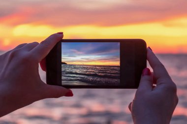Turist elinde akıllı bir telefonla renkli ve güzel bir gün batımının fotoğraflarını çekiyor.