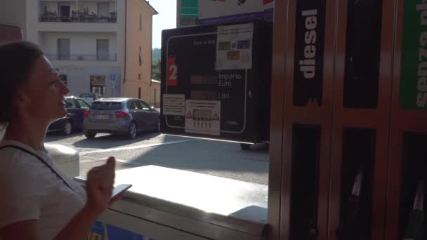Жінка дивиться на панелі ціноутворення на італійській заправній станції — стокове відео