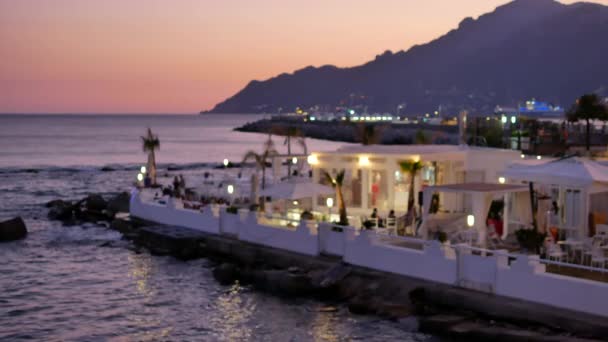 Restaurante iluminado borroso en la orilla del mar y las colinas — Vídeo de stock