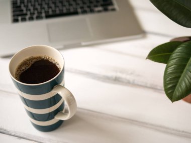 Dizüstü bilgisayar ve büyük kupa ile beyaz ahşap çalışma masası 