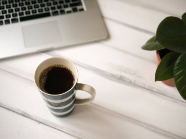 Dizüstü bilgisayar ve büyük bir fincan kahve ile beyaz ahşap çalışma masası