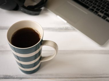Dizüstü bilgisayar, kulaklık ve büyük bir kupa cofee ile ahşap çalışma masası