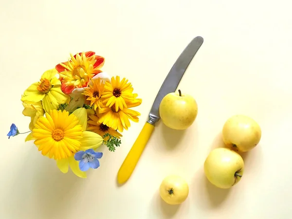 Bouquet of flowers, yellow thread, yellow knife and yellow apples on a yellow background. Garden concept.