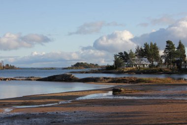 Sand beach, rock formations and house with trees at the back on the shore of Lake Vanern.