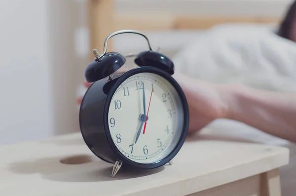 背景に眠っている女性とベッドサイドテーブルの目覚まし時計 — ストック写真