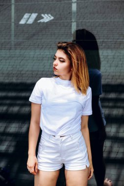 Beyaz bir tişört ve beyaz şort şık kız binanın yakınında duruyor.