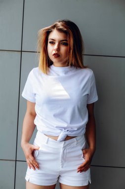 Beyaz bir tişört ve beyaz şort şık kız binanın yakınında duruyor.