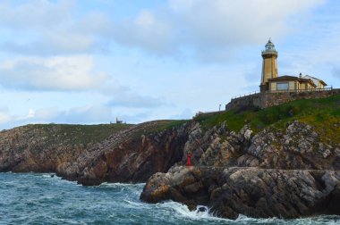 Kayalıkları ve dalgaları olan Rocky sahili. Kayalık uçurumun tepesindeki deniz feneri..