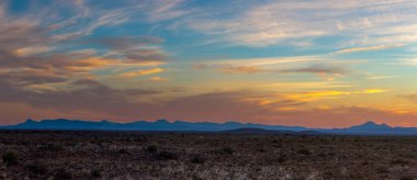 Turuncu renkli bulutlar ve gün batımında mavi dağlar