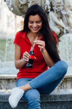 Kırmızı tişörtlü, kola içen güzel ve genç bir kadının fotoğrafını çek.