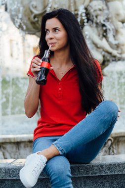Kırmızı tişörtlü, kola içen güzel ve genç bir kadının fotoğrafını çek.
