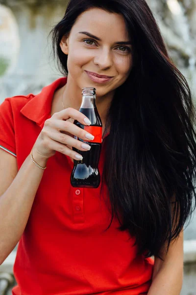 Kırmızı tişörtlü, kola içen güzel ve genç bir kadının fotoğrafını çek.