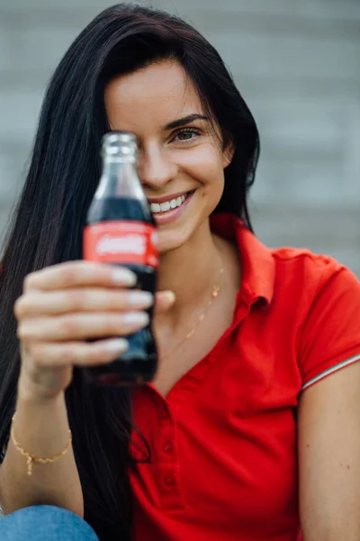 Kırmızı tişörtlü, kola içen güzel ve genç bir kadının fotoğrafını çek.