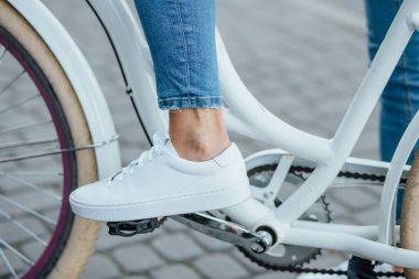 Bisiklet pedalında beyaz spor ayakkabı ve kot pantolon.